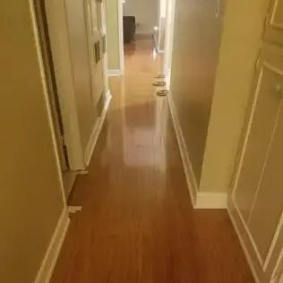 Narrow hallway with hardwood floor, beige walls, and a few small objects along the right side.