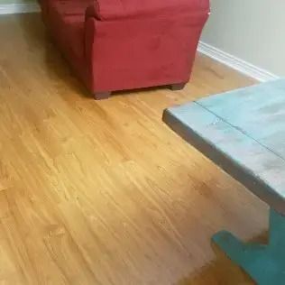 Living room with red armchair, hardwood floor, and corner of a glass table