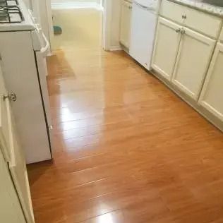 Narrow kitchen with light wood floor, white cabinets, and appliances along both sides