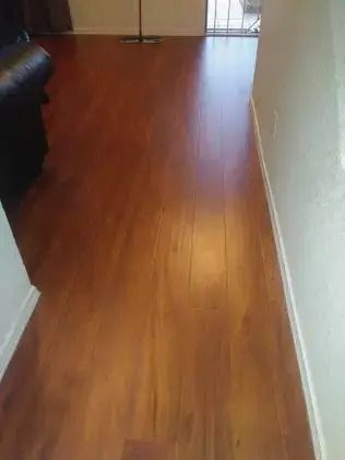 Empty hallway with polished wooden floor and white walls, leading to a glass door at the end.