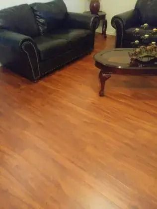 Living room with black leather sofas, a glass coffee table, and hardwood floors
