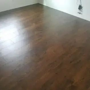 Empty room with dark hardwood floors and white walls, sunlit from a window on the left.
