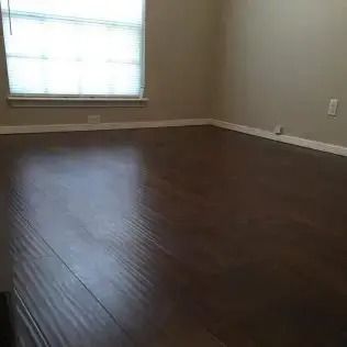Empty room with dark hardwood floors, beige walls, and a window with blinds.