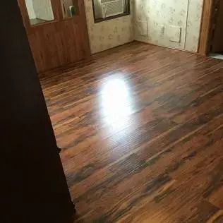 Empty room with wood-look flooring, worn wallpaper, and a bright reflection on the floor