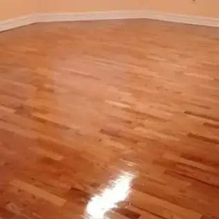 Empty room with glossy hardwood floor and white baseboards, reflecting light