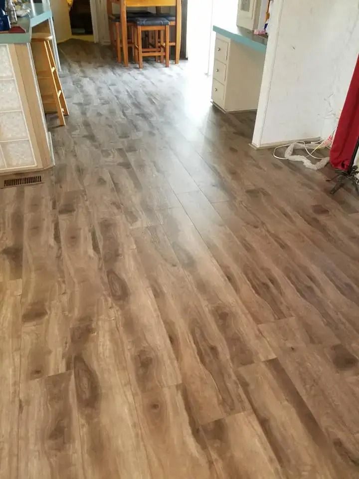 Empty hallway with wood-look flooring, kitchen cabinets, and a dining table in the background