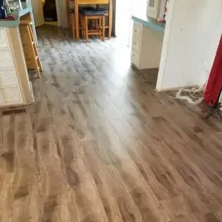 Empty hallway with wood-look flooring leading to a dining area and kitchen.