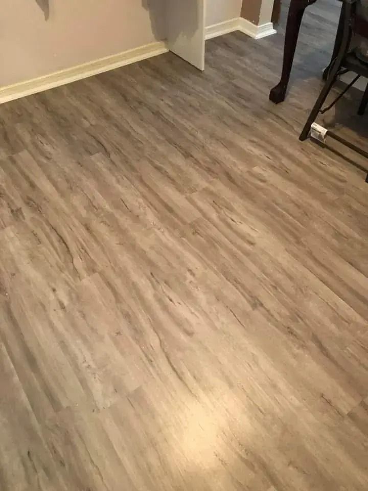 Empty wood-look floor in a room with beige walls and a small table leg visible on the right.