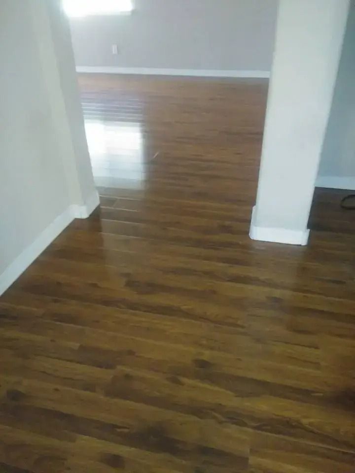 Empty room with glossy hardwood floors, white walls, and a doorway opening into a bright hall