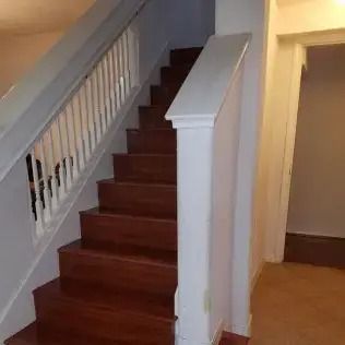 Staircase with dark wood steps, white railing, and an open doorway in a hallway.