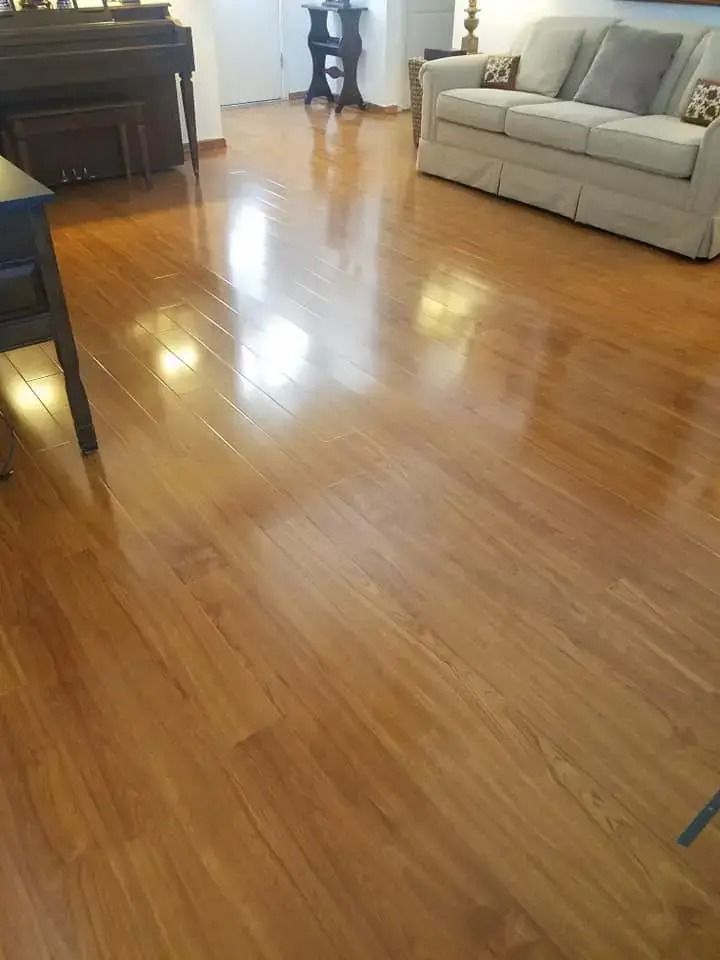 Bright living room with shiny hardwood floor, gray sofa, and piano in the corner.