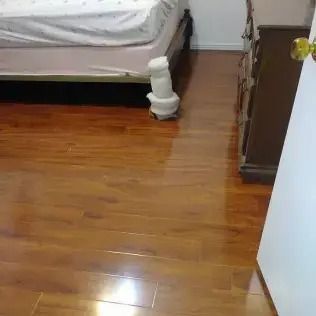 Bedroom with a bed, wooden floor, and a small white pet sitting near the bed corner.