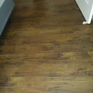 Wooden floor in a hallway with white walls and a doorway visible.