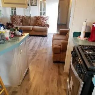 Small kitchen opening into a living room with a beige couch, wood floor, and a gas stove in the foreground