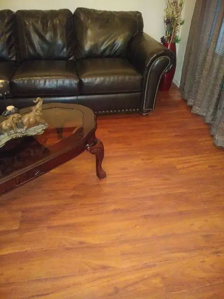 Living room with a black leather sofa, glass coffee table, and wood flooring