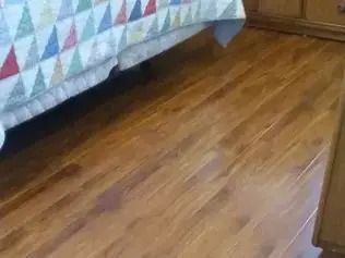 Wooden floor beside a bed with a colorful quilt and a small dresser