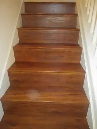 Wooden staircase with a reddish-brown finish, viewed from the bottom indoors.