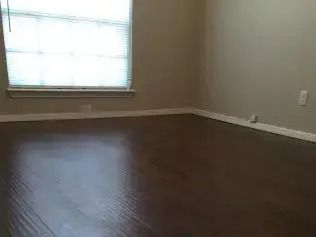 Empty room with hardwood floors, beige walls, and a window with blinds.