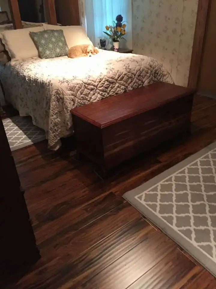 Cozy bedroom with a bed, wooden chest at the foot, and patterned rug on dark wood flooring
