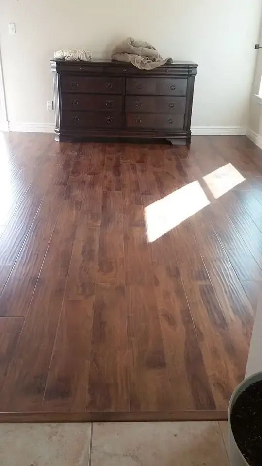 Empty hardwood-floored room with a dark dresser against the far wall and sunlight on the floor.
