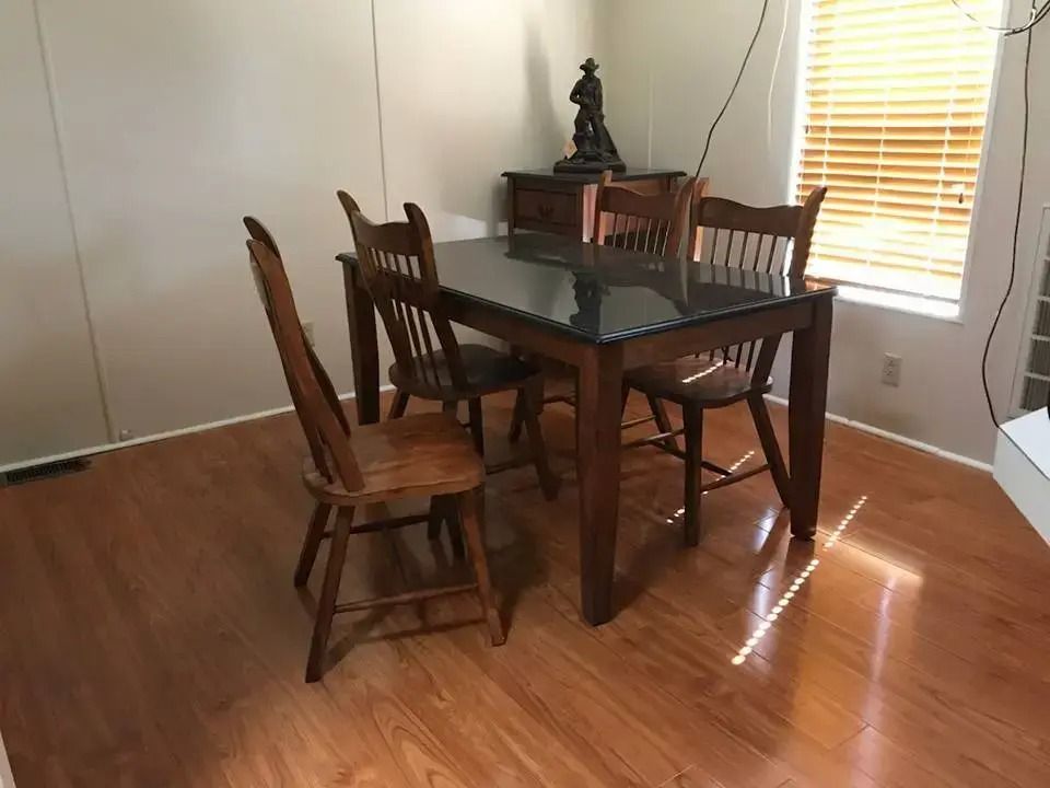 Dining table with four wooden chairs in a sunlit room, beside a window and glass door.