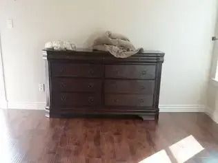 Dark wooden dresser against a white wall in an empty room with hardwood floors.