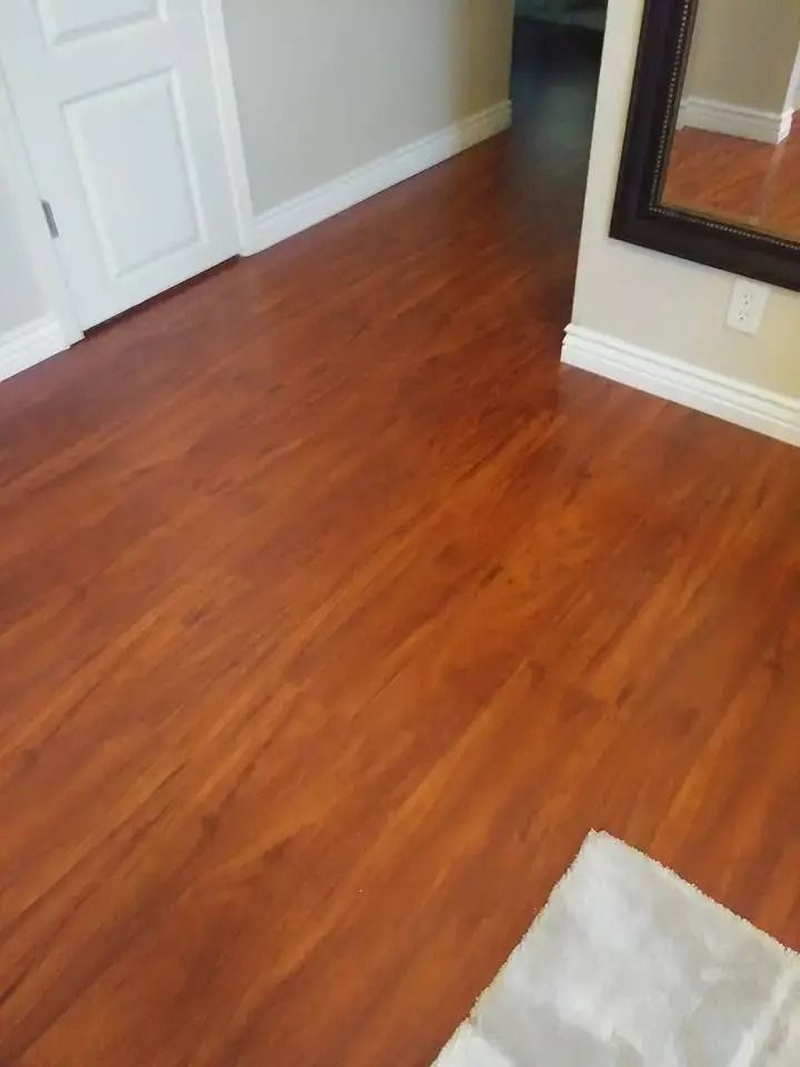 Empty room with reddish-brown hardwood floor, white walls, and a fireplace edge visible on the right.