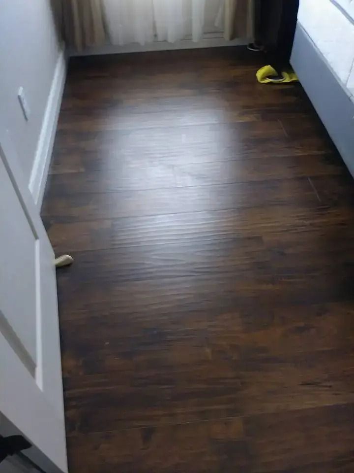 Small empty room with dark wood floor, white door, and curtains at the far end.