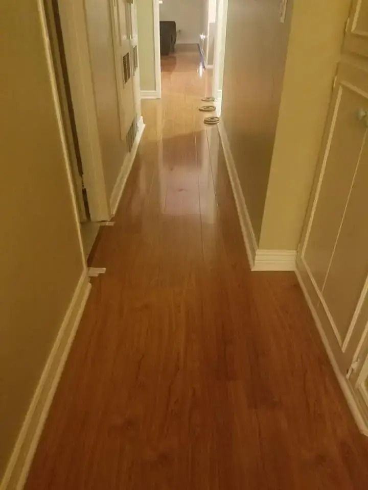 Narrow hallway with hardwood floors and beige walls, seen from one end toward a doorway.