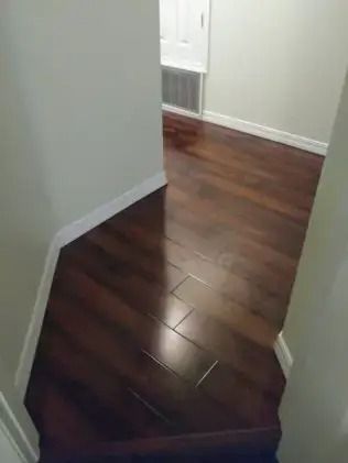 Narrow hallway with dark hardwood floor and white walls, leading to a brighter room.