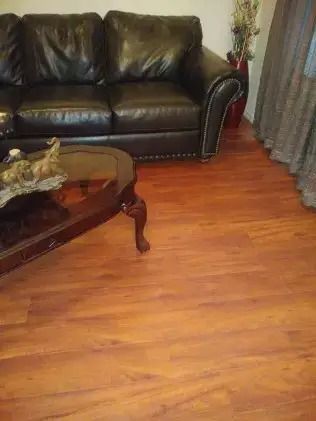 Living room with black leather sofa, wooden coffee table, and hardwood floor near curtains.