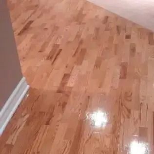 Shiny hardwood floor corner with light walls and white baseboard trim