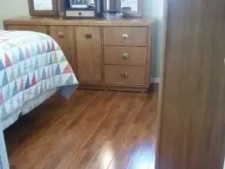 Bedroom with wood floor, bed with quilt, and wooden dresser by a wall.