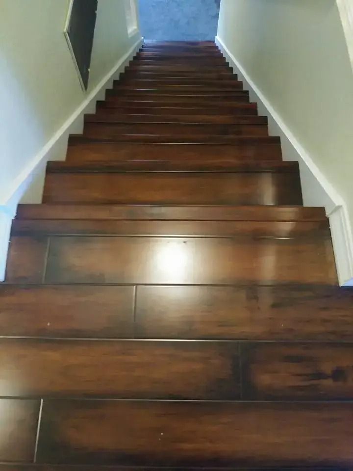 Wooden staircase with dark steps and white walls, viewed from the bottom looking upward.