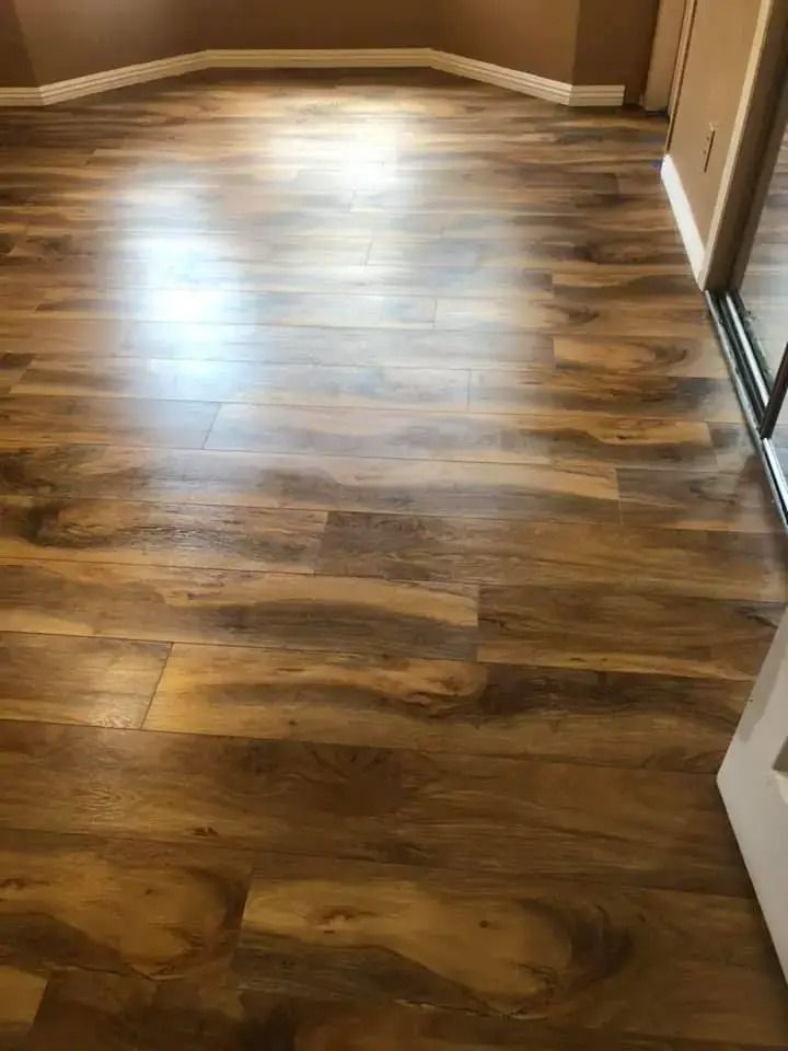 Empty room with wood-look flooring and brown walls, lit by sunlight from a doorway.