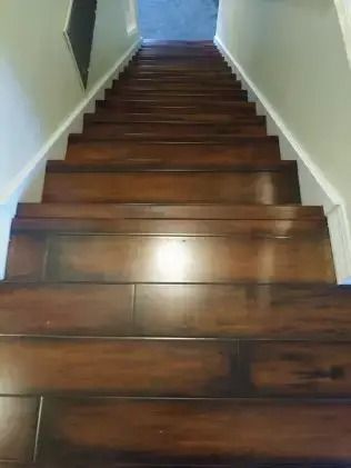 Wooden staircase with dark steps and white walls, viewed from the bottom looking upward.