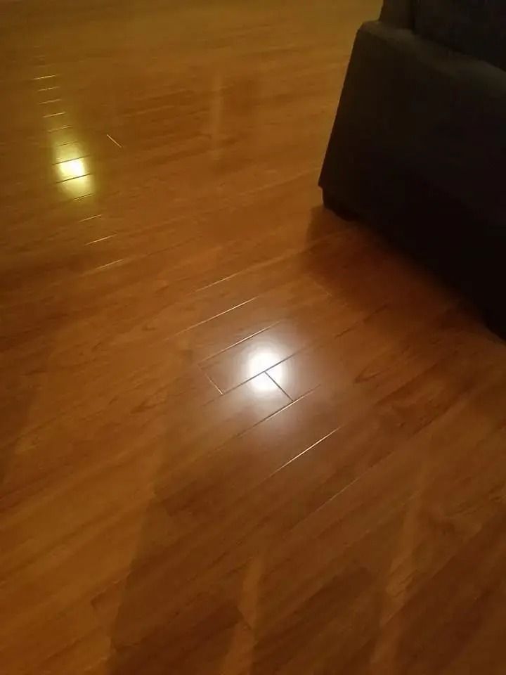 Glossy wooden floor reflecting light beside a dark couch corner