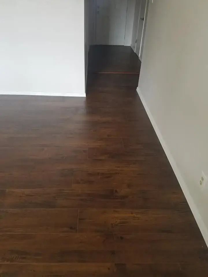 Empty room with dark wood flooring, white walls, and a hallway opening ahead