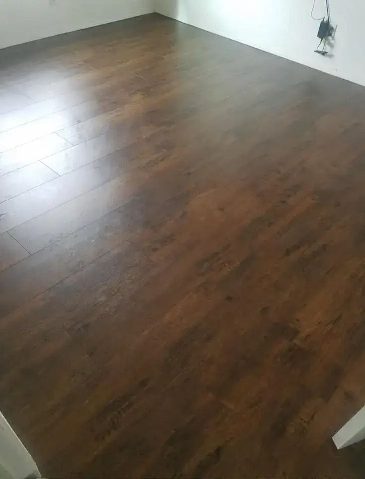 Empty room with dark wood flooring and white walls, with a small wall outlet visible.