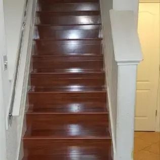 Wooden staircase with dark polished steps and white walls, leading up to a hallway with a closed door.