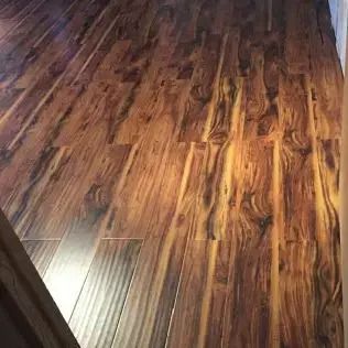 Wood-look laminate flooring with warm brown grain and a bright reflection in the lower left corner