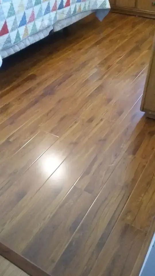 Wooden bedroom floor beside a bed with a quilted blanket and dresser