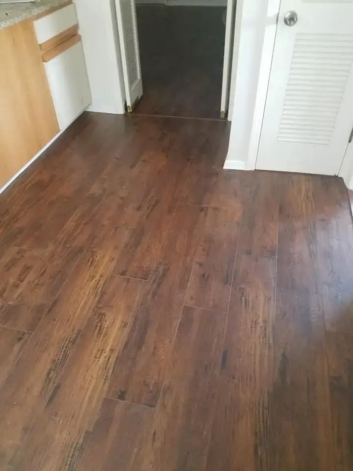 Wooden kitchen floor leading to a hallway, with white cabinets and closet doors nearby.