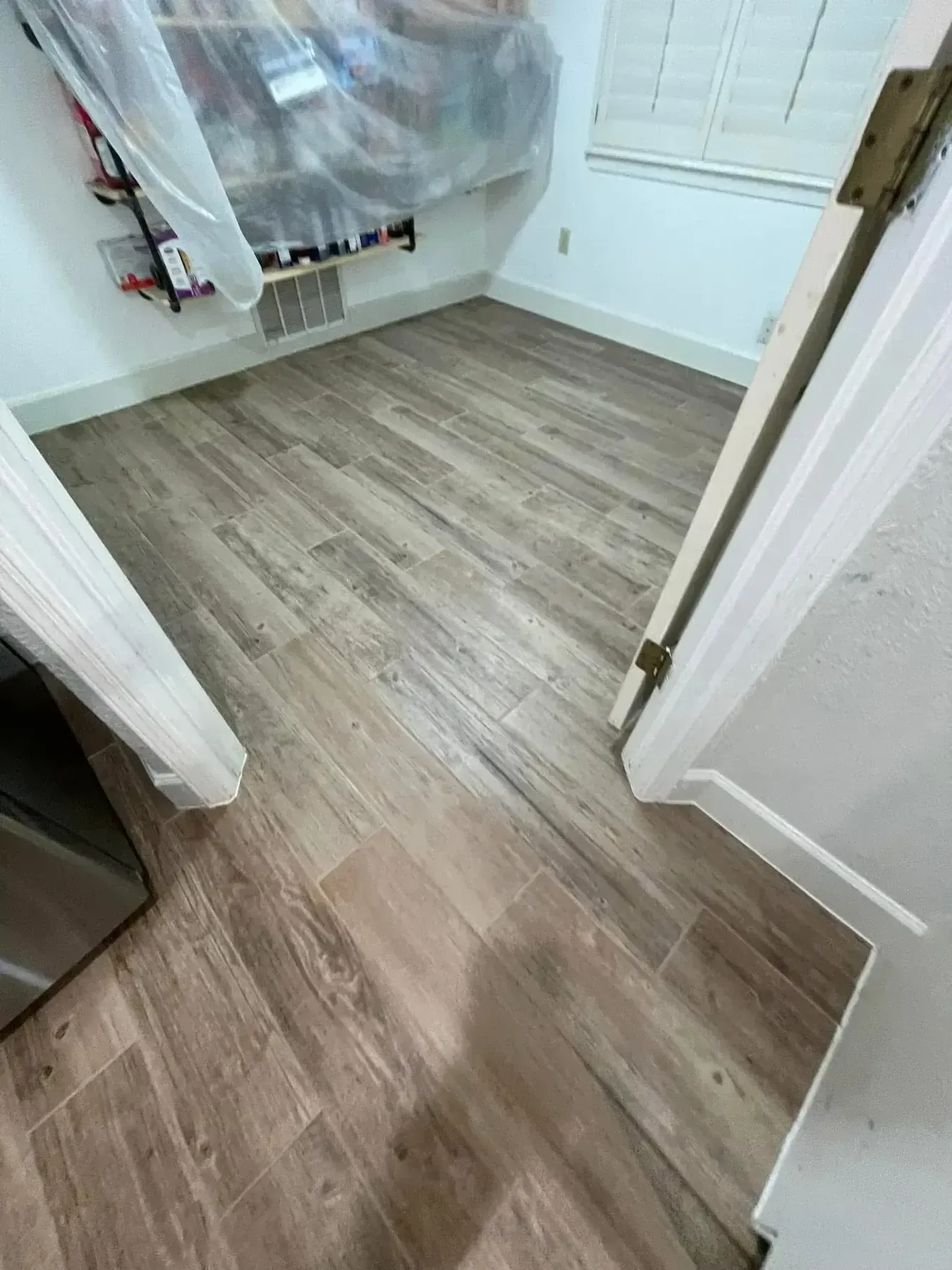 Small hallway with wood flooring leading into a closet with plastic-covered items and white walls.
