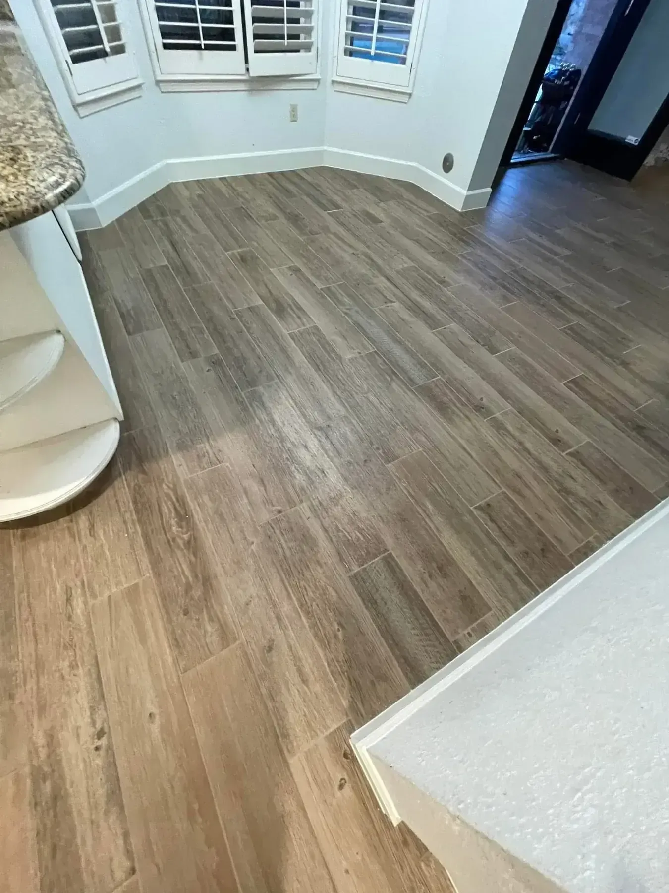 Empty room with wood-look flooring, white walls, and windows with shutters.