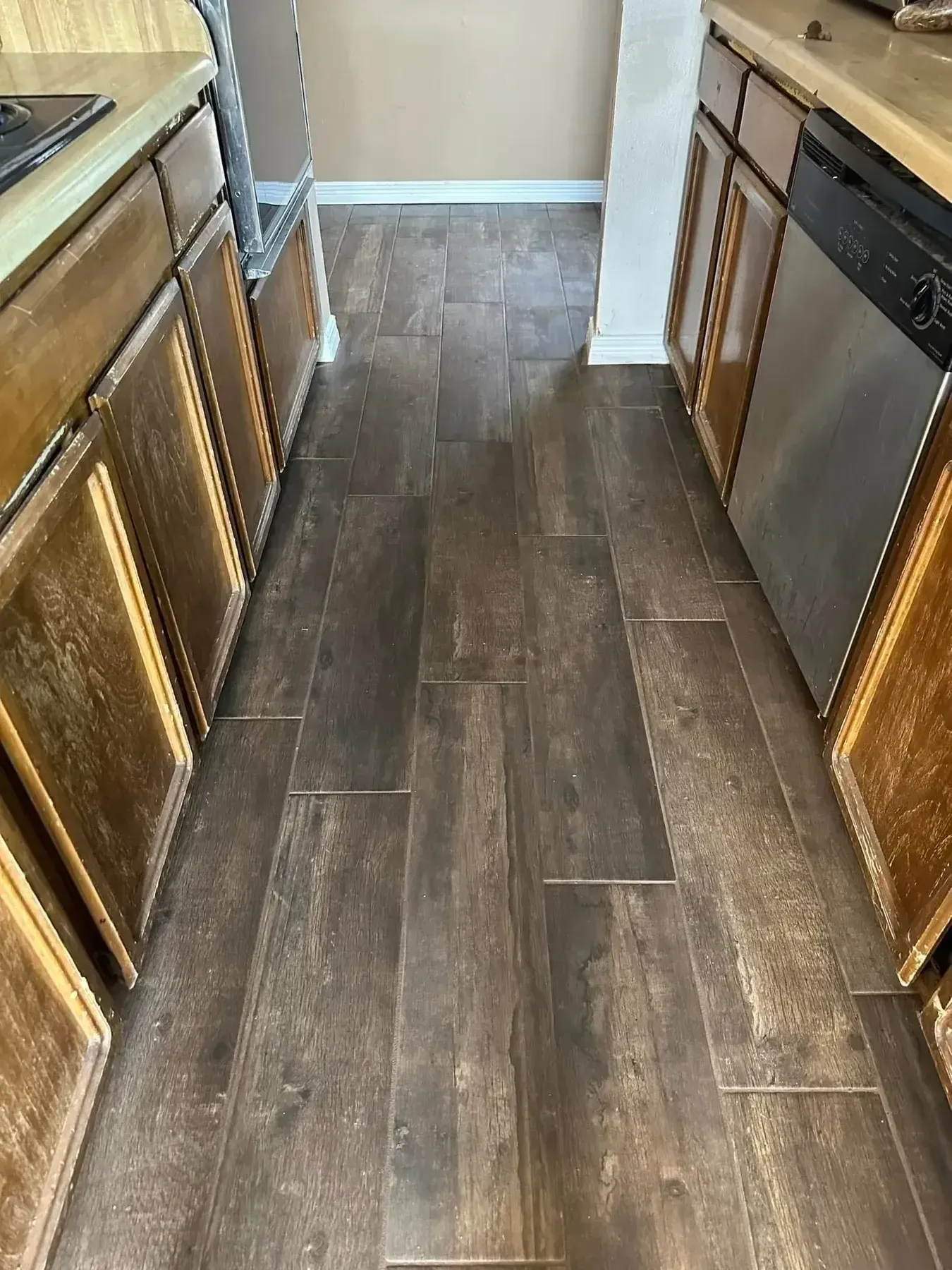 Kitchen hallway with wood-look tile flooring, wood cabinets, and stainless steel appliances on both sides