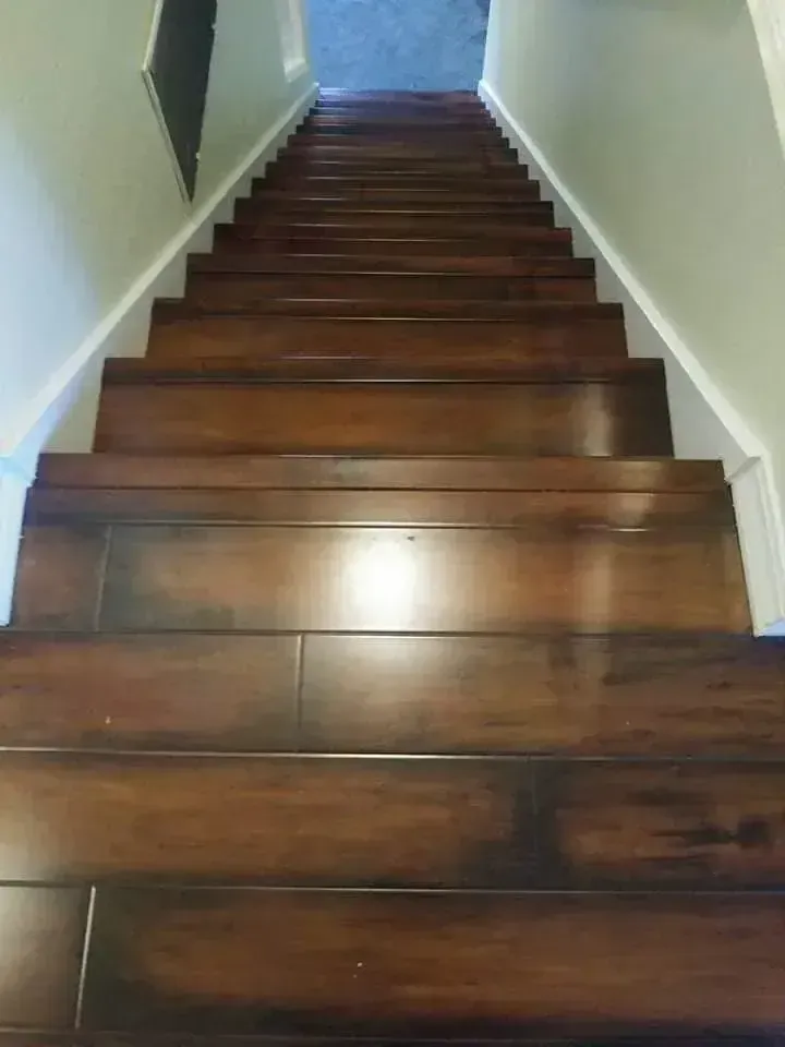 Wooden staircase with dark steps and white walls, viewed from the bottom looking up.