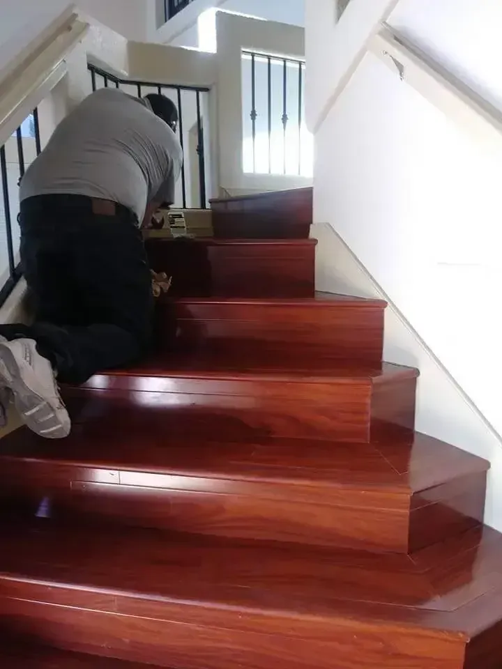 Person crawling up glossy wooden stairs indoors, with white walls and railing.