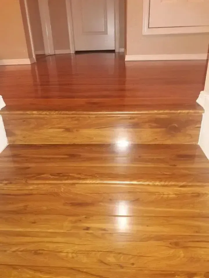 Shiny hardwood staircase leading to a hallway with white doors and beige walls