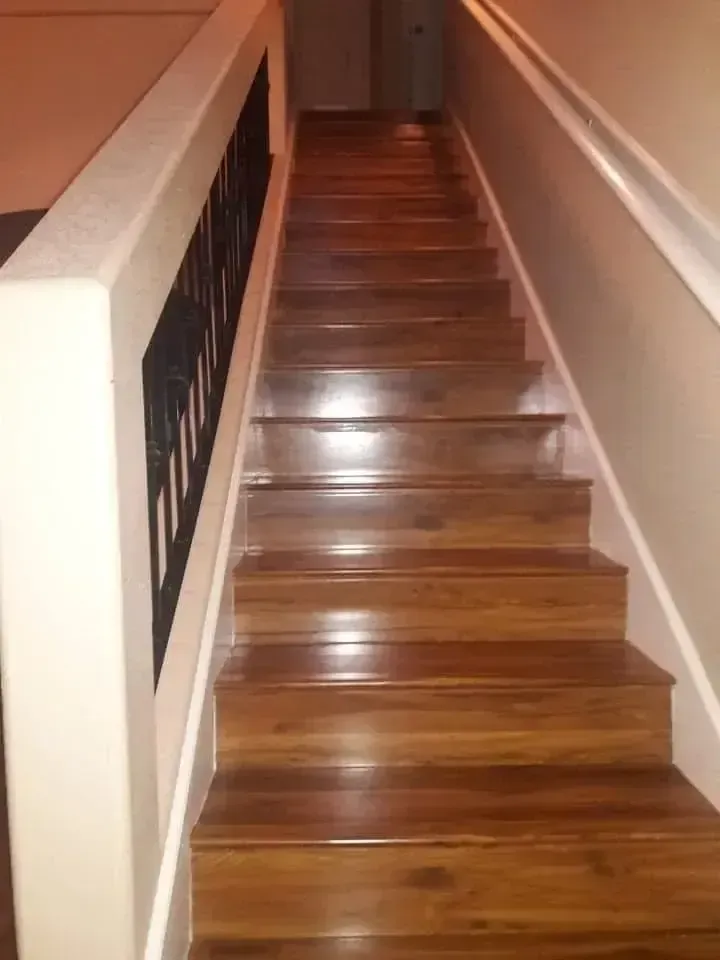 Wooden staircase in a narrow hallway with white walls and a dark railing.